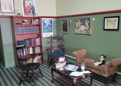 an interior of a room in Yiddishland filled with paintings on the wall, books on a shelf, and furniture